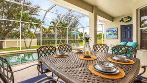 Zona pranzo con vista sulla piscina, sedute all'aperto e una parete decorativa.