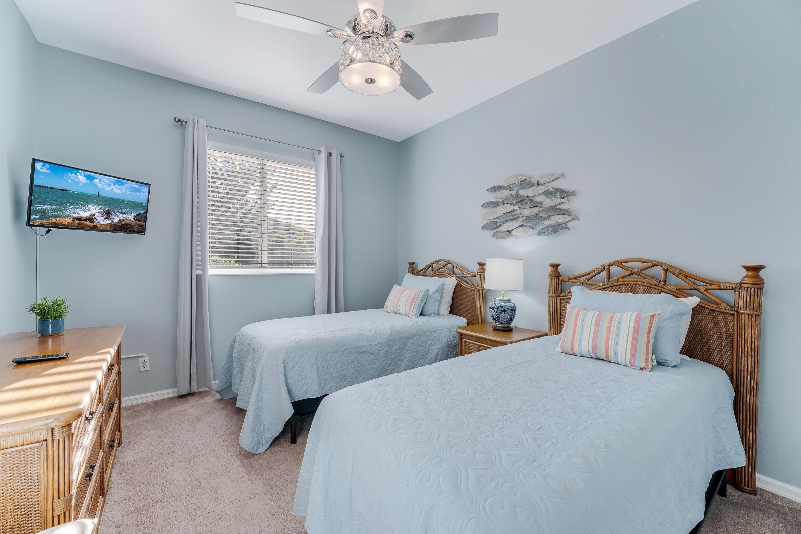 A bedroom with two beds, a ceiling fan, a TV, a window with blinds, and a wall decoration.