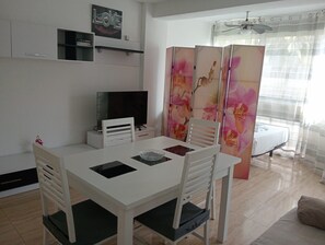 Ett modernt matområde med ett vitt bord, stolar, en tv och en dekorativ avskärmning med blommönster.