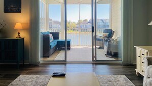 A spacious living area with a sliding glass door leading to a balcony overlooking a body of water and residential buildings. - 3BR/Game Room/Pool/Outdoor Sports/3 miles to DE and MD Beaches (Selbyville)