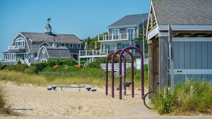 Una casa sulla spiaggia con un'ampia veranda, una bicicletta e una zona di spiaggia sabbiosa.