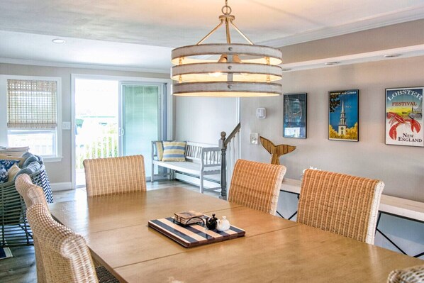 A dining area with a wooden table, wicker chairs, and a hanging light fixture.