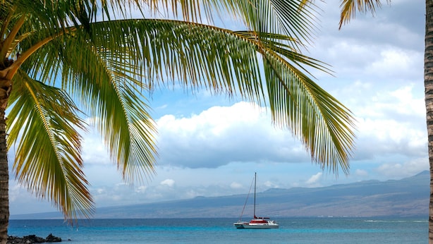 A beach with a single lounge chair, clear blue water, a sailboat, and a mountain range in the distance. - Luxury Stay w/ Private Beach Club, Hilton Pool Passes, Sunset Views (Waimea)
