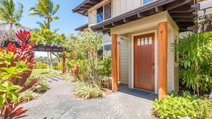 A house with a wooden porch, a front door, and a garden with various plants. - Luxury Stay w/ Private Beach Club, Hilton Pool Passes, Sunset Views (Waimea)