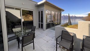 A modern outdoor patio with glass doors and a view of a lake and mountains. - Iconic Queenstown Apartment (Queenstown)