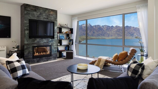 A modern living room with a fireplace, a large TV, a comfortable seating area with a view of mountains and a lake. - Iconic Queenstown Apartment (Queenstown)