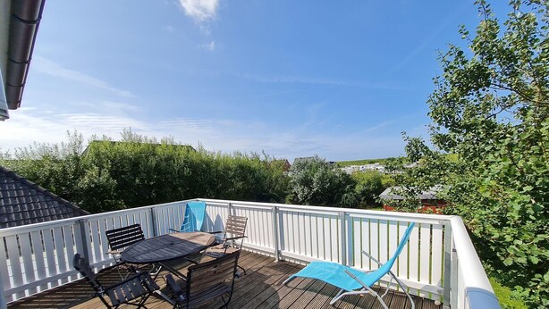 Une terrasse en bois avec une balustrade blanche, une table, deux chaises et un parasol bleu.