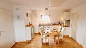 Une cuisine de taille réduite avec un coin repas, un plancher en bois et des meubles de cuisine blancs.