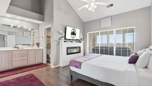 A bedroom with a bed, a fireplace, a ceiling fan, and a large window. - Golf Course Escape • 3BR Legacy Condo w/ Fireplace & Sunroom (Branson)