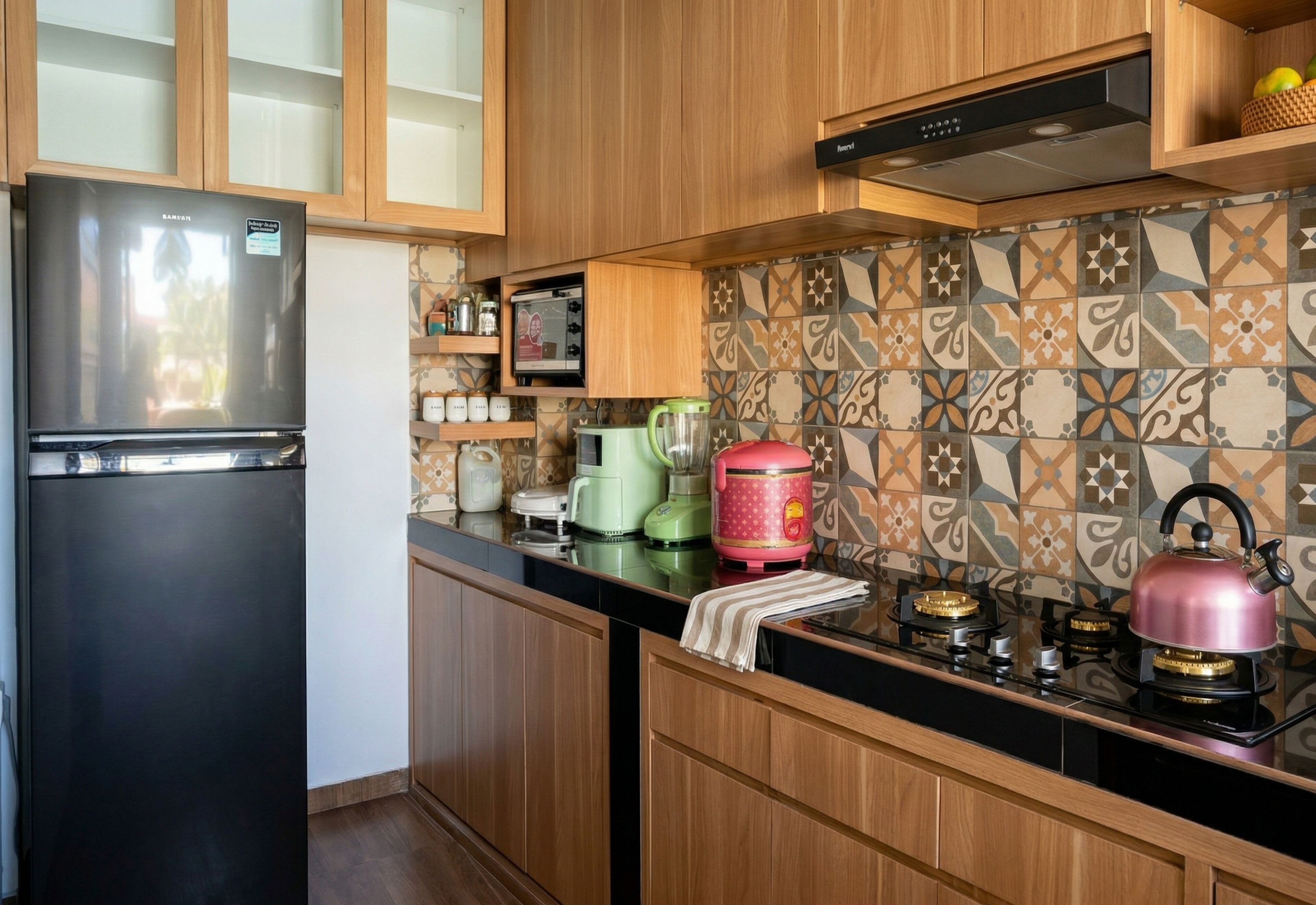 Una cocina con armarios de madera, un refrigerador negro, un microondas, una tetera y un salpicadero con diseño.