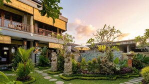 A courtyard with a stone pathway, lush greenery, and a building with a balcony. - Sari Murni (Ubud)