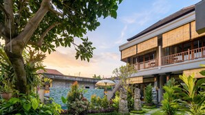 A courtyard with a stone pathway, lush greenery, and a building with a balcony. - Sari Murni (Ubud)