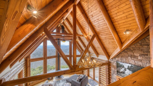 A log cabin interior with a stone fireplace, a chandelier, and a large window offering a mountain view. - EPIC VIEWS-HotTub-WoodStove-Sauna-Fireplace-GameRoom-Playset-EV-FencedYard+More! (Rosman)