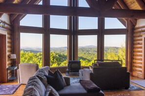 L’intérieur d’une cabane en rondins, avec une grande fenêtre donnant sur un paysage boisé.