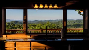A kitchen with a view of a forested mountain range through large windows.