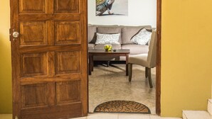 An open wooden door leading to a living room with a sofa, a coffee table, and a painting on the wall. - Aspid Studio & Apartment (Oranjestad)