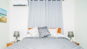A bedroom with a bed, two bedside lamps, a wall-mounted air conditioner, and a curtain. - Aspid Studio & Apartment (Oranjestad)