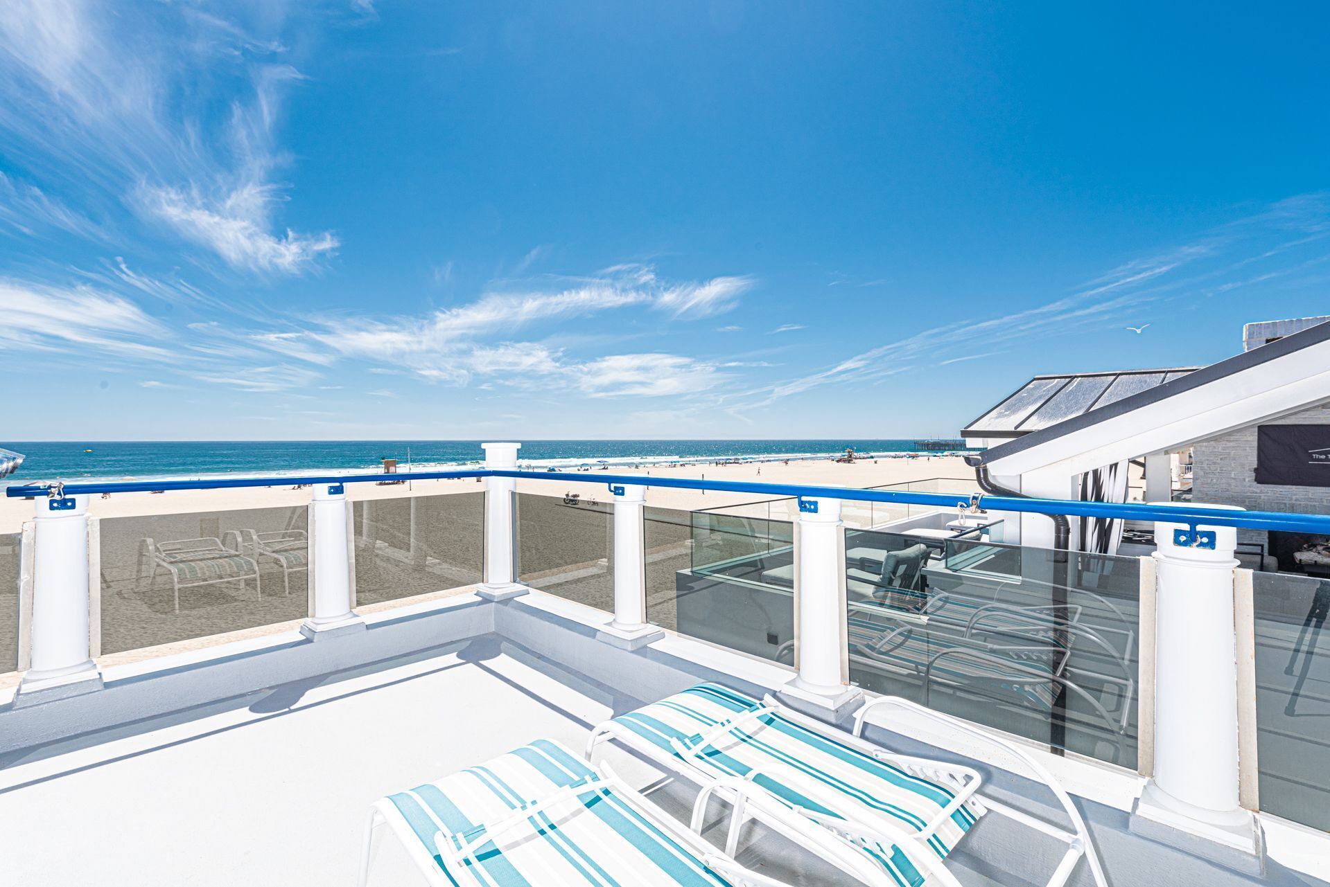 A sun deck with lounge chairs, a glass balustrade, and a view of the beach and ocean.