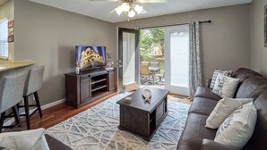 Ein Wohnzimmer mit einem dunkelbraunen Ledersofa, einem Couchtisch, einem Fernseher auf einem Holzständer und einem gemusterten Teppich.
