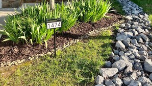 Ein Haus mit Steinaußenwand, einem einladenden Schild und einem gepflegten Garten mit Steingrenze und Grünpflanzen.
