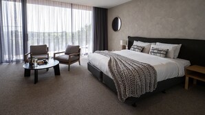 A hotel room with a large bed, a seating area with a table, and a view of the outdoors. - Links Lodge at The Dunes (Rye)