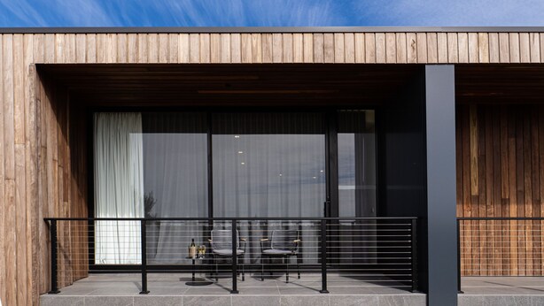 A modern building with a wooden facade, large sliding glass doors, and a balcony with a metal railing. - Links Lodge at The Dunes (Rye)