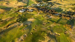 An aerial view of a golf course with a clubhouse and a large building with a solar panel roof. - Links Lodge at The Dunes (Rye)