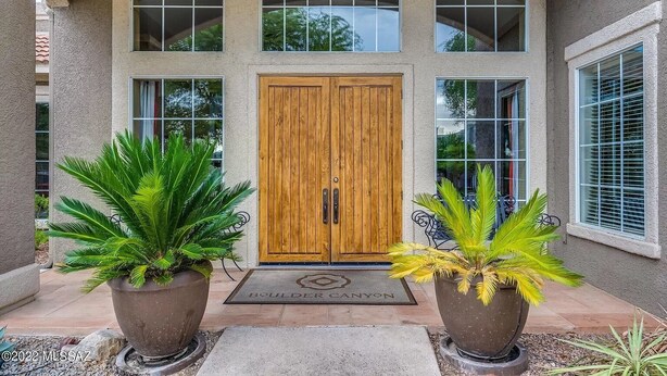 Una casa de dues plantes amb una porta de fusta, grans finestres i plantes en test amb al davant.