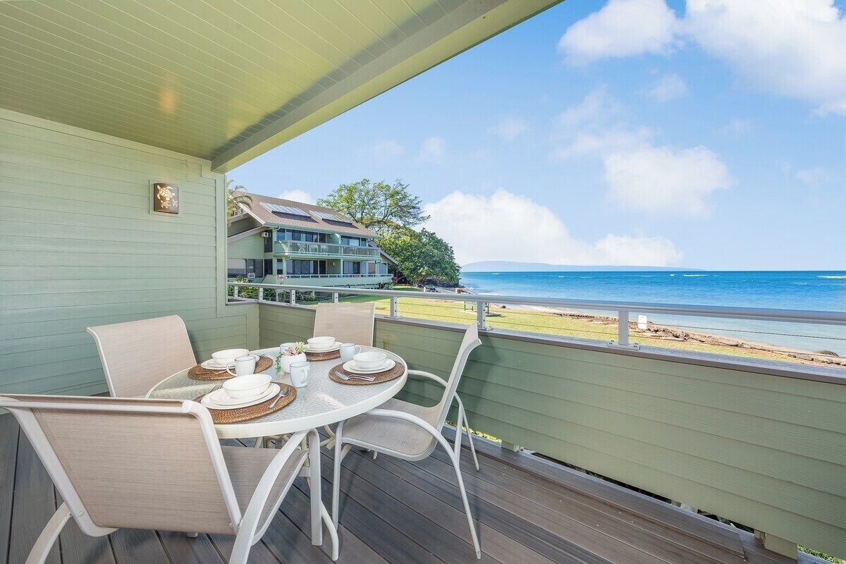 Un espacio comedor al aire libre techado con una mesa preparada para cuatro, con vistas a una playa y al océano.