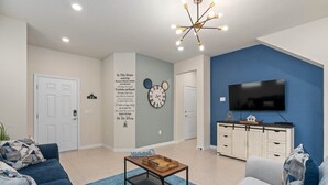 Una sala de estar con una pared azul, un televisor montado, una mesa de centro y un sofá.