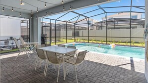 Un patio exterior con piscina, una mesa y sillas.