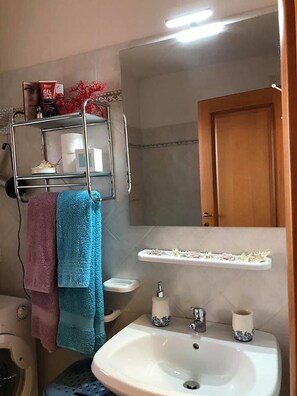 A bathroom with a white sink, a shelf with toiletries, and a door. - Sweet Home ISOLA ROSSA (Trinita d'Agultu)