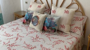 Ein Bett mit einer blumigen Tagesdecke, einem Rattan-Kopfstück und Zierkissen mit Meeresmotiven.