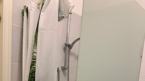 A shower area with a glass door, a towel rack with a white towel and a green leaf-patterned towel, and a showerhead. - Sweet Home Mare Li FERULI (Trinita d'Agultu)