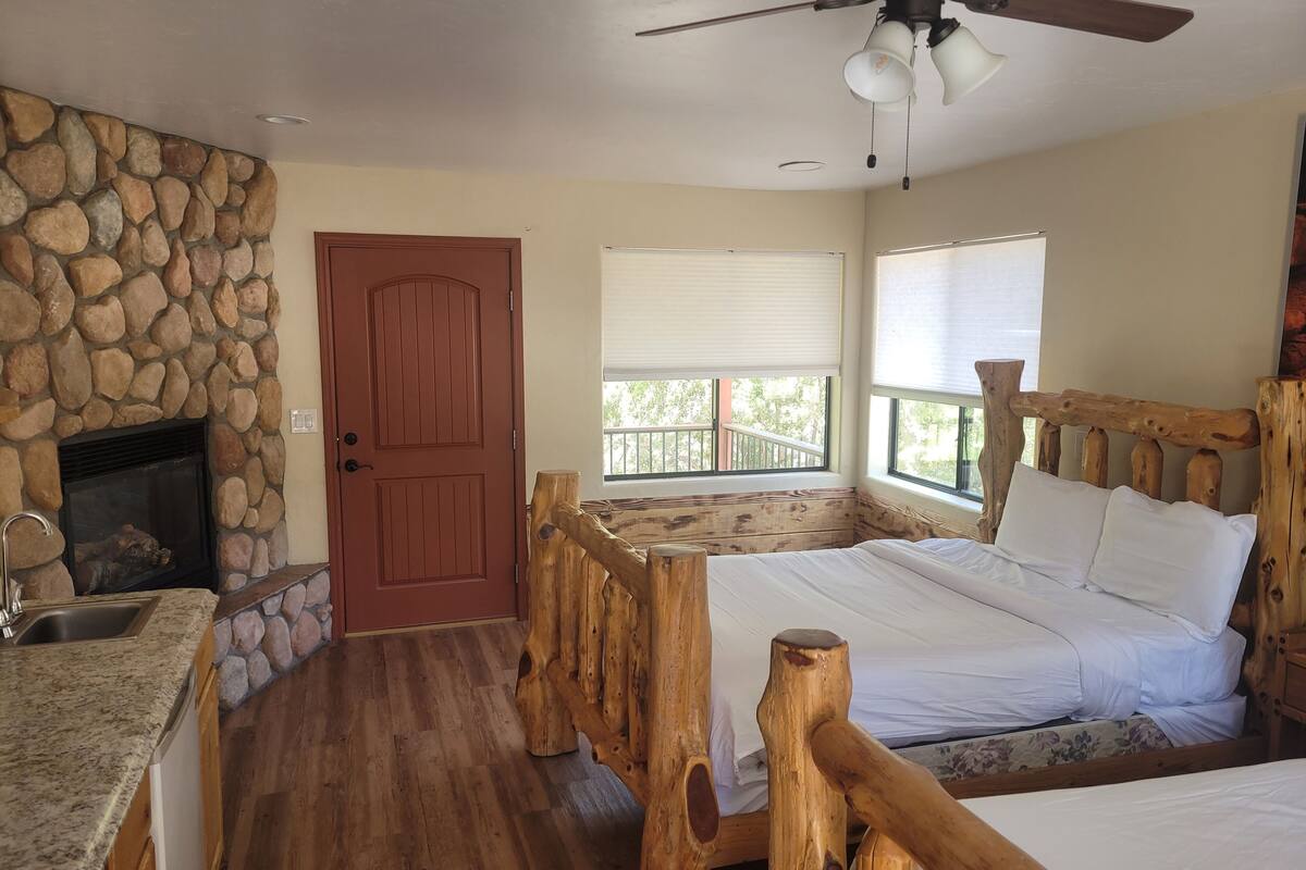 A bedroom with a stone fireplace, wooden bed frame, and a balcony with a view.