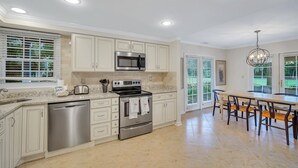 A modern kitchen with stainless steel appliances, a dishwasher, and a dining area with a long table and chairs. - 276 Evian: Newly renovated single story unit with golf course views and tennis court access! (Hilton Head Island)