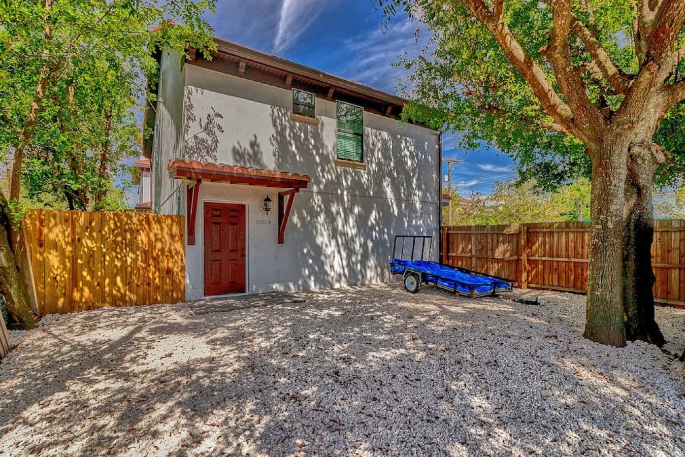 A single-story building with a red door, a small attached garage, and a gravel driveway.