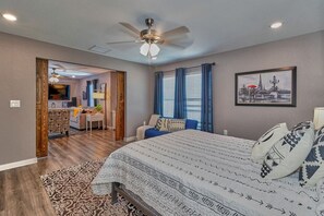 Une chambre à coucher avec un lit, un bureau et une chaise. Il y a un ventilateur de plafond et une fenêtre avec des rideaux.