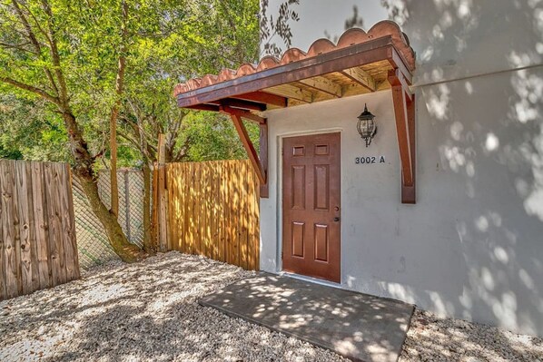 Un edificio con puerta de madera, el número '3002 A' en la pared y una pérgola con techo de tejas.