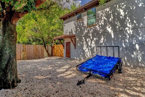 Un espacio al aire libre cubierto con un lona azul, una valla de madera y un edificio con puerta y ventanas.