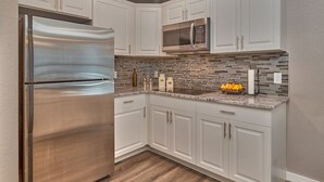 A kitchen with white cabinets, a stainless steel refrigerator, a microwave, and a stone backsplash.