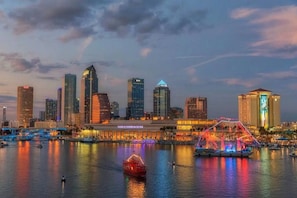 Une vue panoramique de la ville, avec des bâtiments illuminés et une zone riveraine où l’on aperçoit des bateaux et une grande roue.