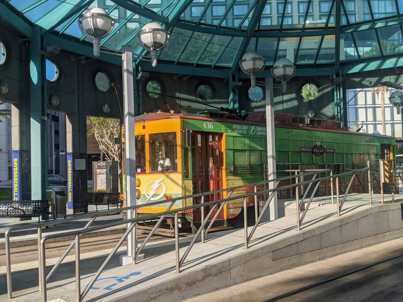 Una estación de tranvía con techo de vidrio, bancos y un tranvía con el número 436.