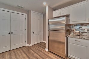 Una cocina con armarios blancos, un refrigerador de acero inoxidable y suelo de madera.
