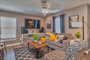 Ein Wohnzimmer mit grauem Sofa, einem gemusterten Ottomanen und einem Couchtisch mit Dekoration.