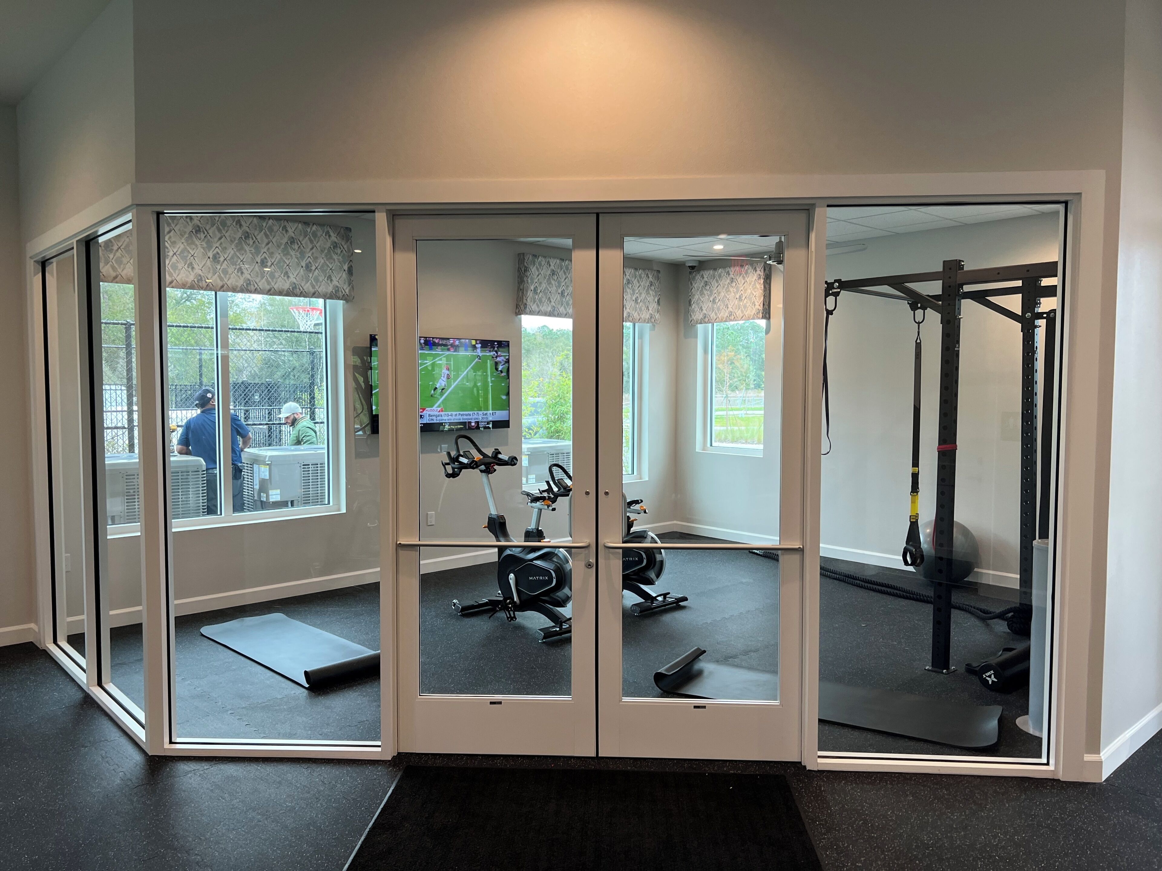 Ein Fitnessraum mit Spiegelwänden, Trainingsgeräten und großen Fenstern.