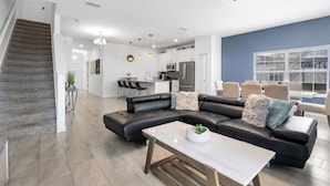 A modern living room with a black leather sofa, a white coffee table, and a kitchen in the background.