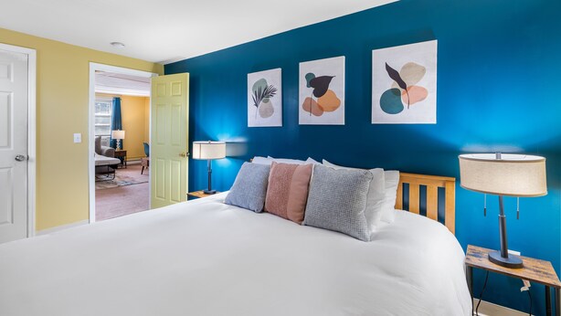 Un dormitorio con una cama grande, una mesita de noche con lámpara y tres obras de arte abstracto en la pared.