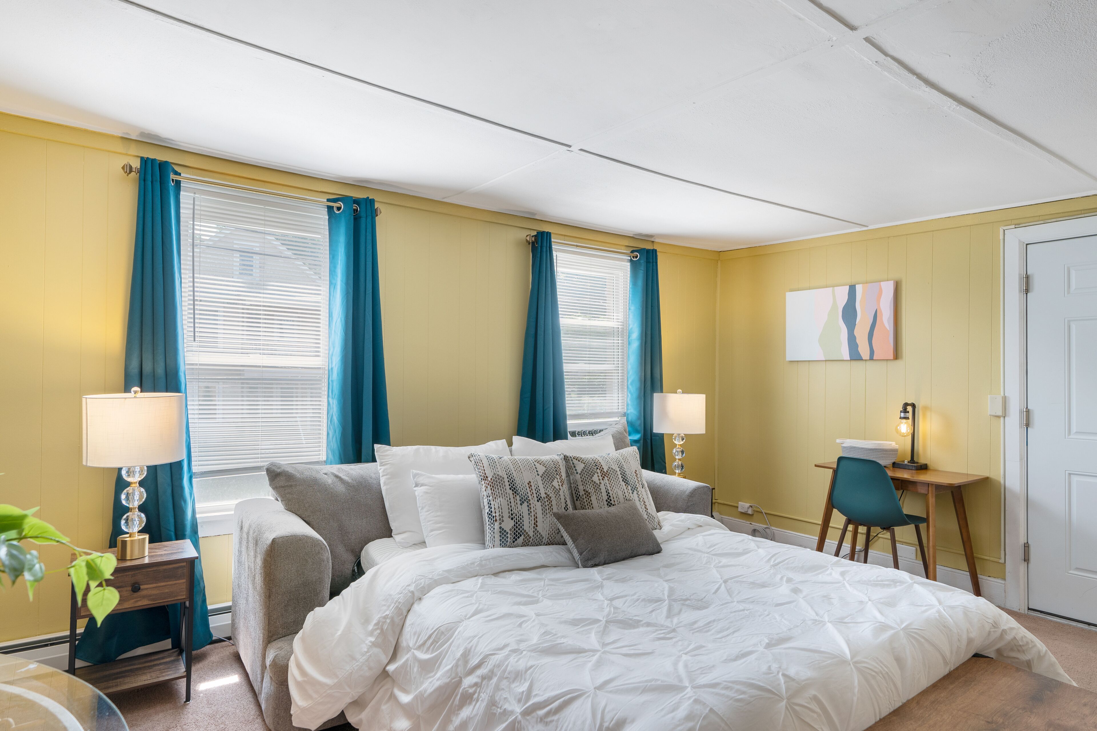 Une chambre à coucher comprenant un lit, deux tables de chevet avec des lampes, une chaise et un bureau avec une lampe.