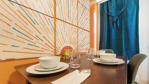 Una mesa de comedor dispuesta con cuencos, platos y cubiertos blancos, una jarrón y vasos.